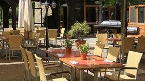 Un área de comedor al aire libre con sillas y mesas de mimbre, plantas en macetas y una parrilla.