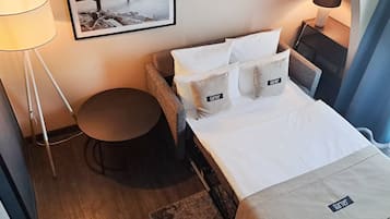 A hotel room with a bed, a round table, a lamp, and a framed picture on the wall.