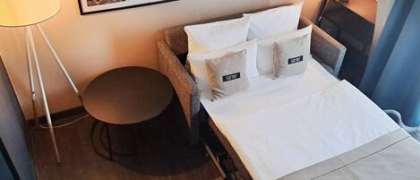 Une chambre d’hôtel avec un lit, une table ronde, une lampe et un tableau encadré au mur.