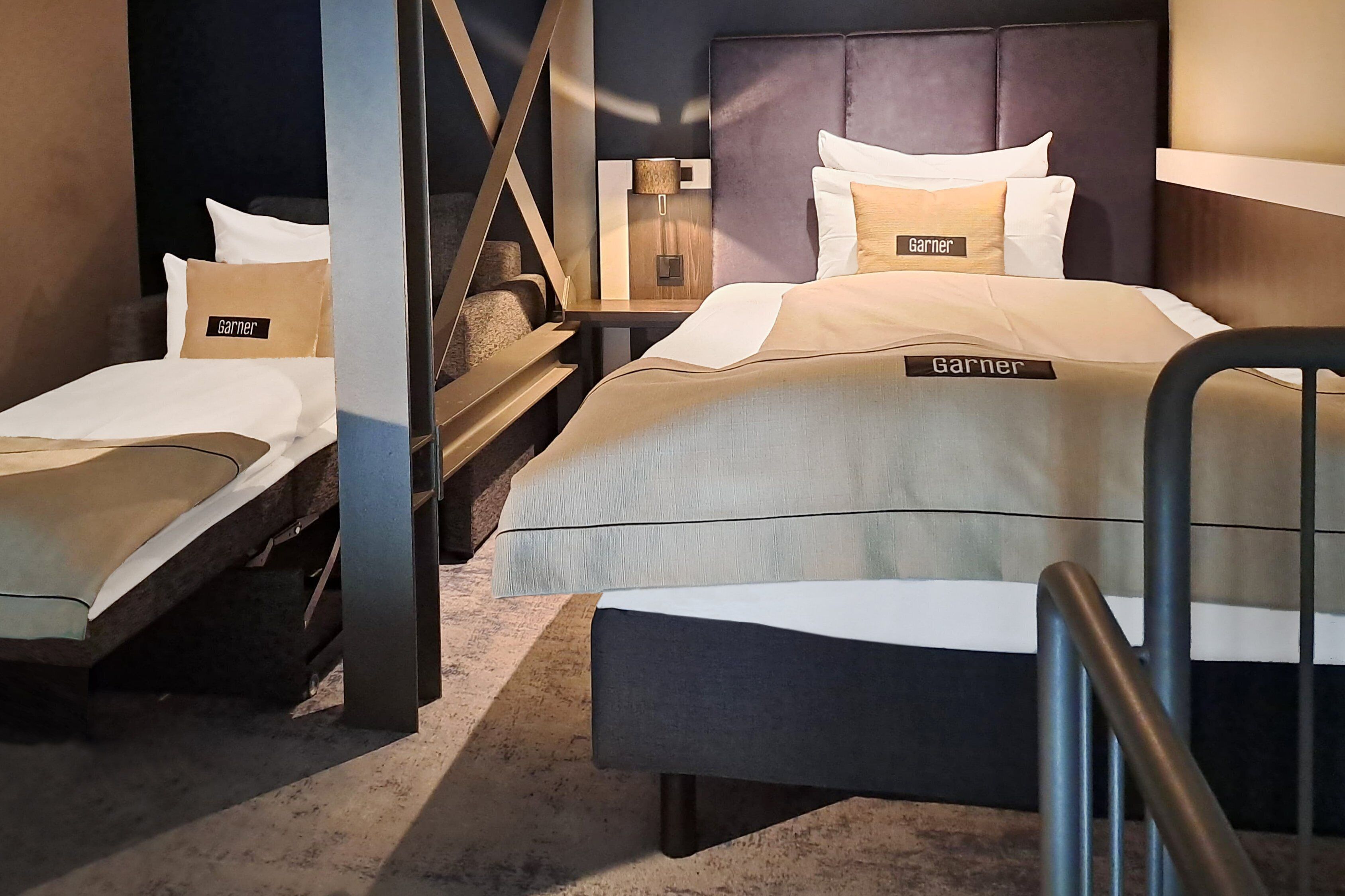 Ein Hotelzimmer mit zwei Betten, einem Nachttisch, einer Lampe und einer Treppe.
