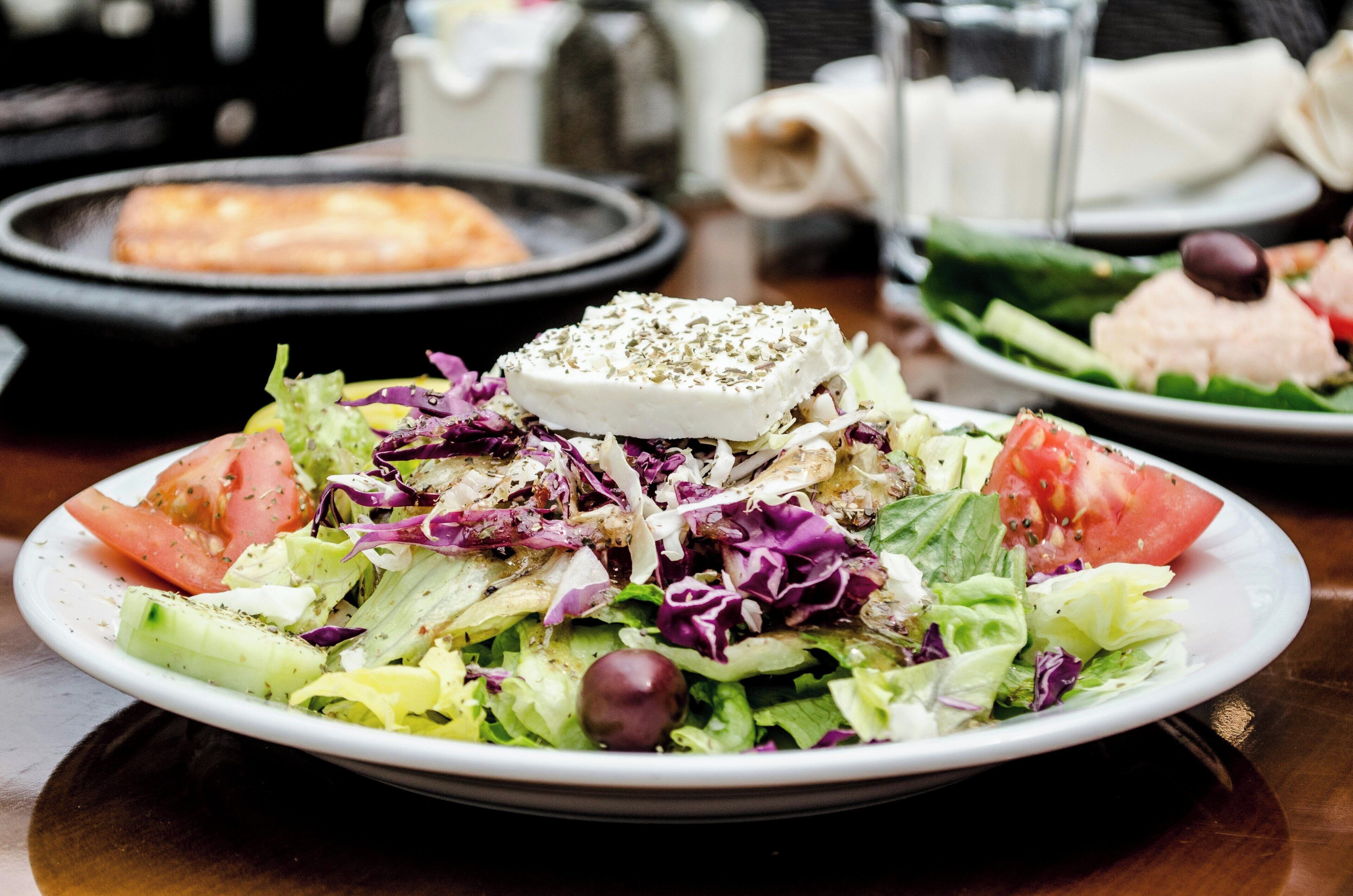 A plate of salad with various vegetables and a piece of cheese on top.