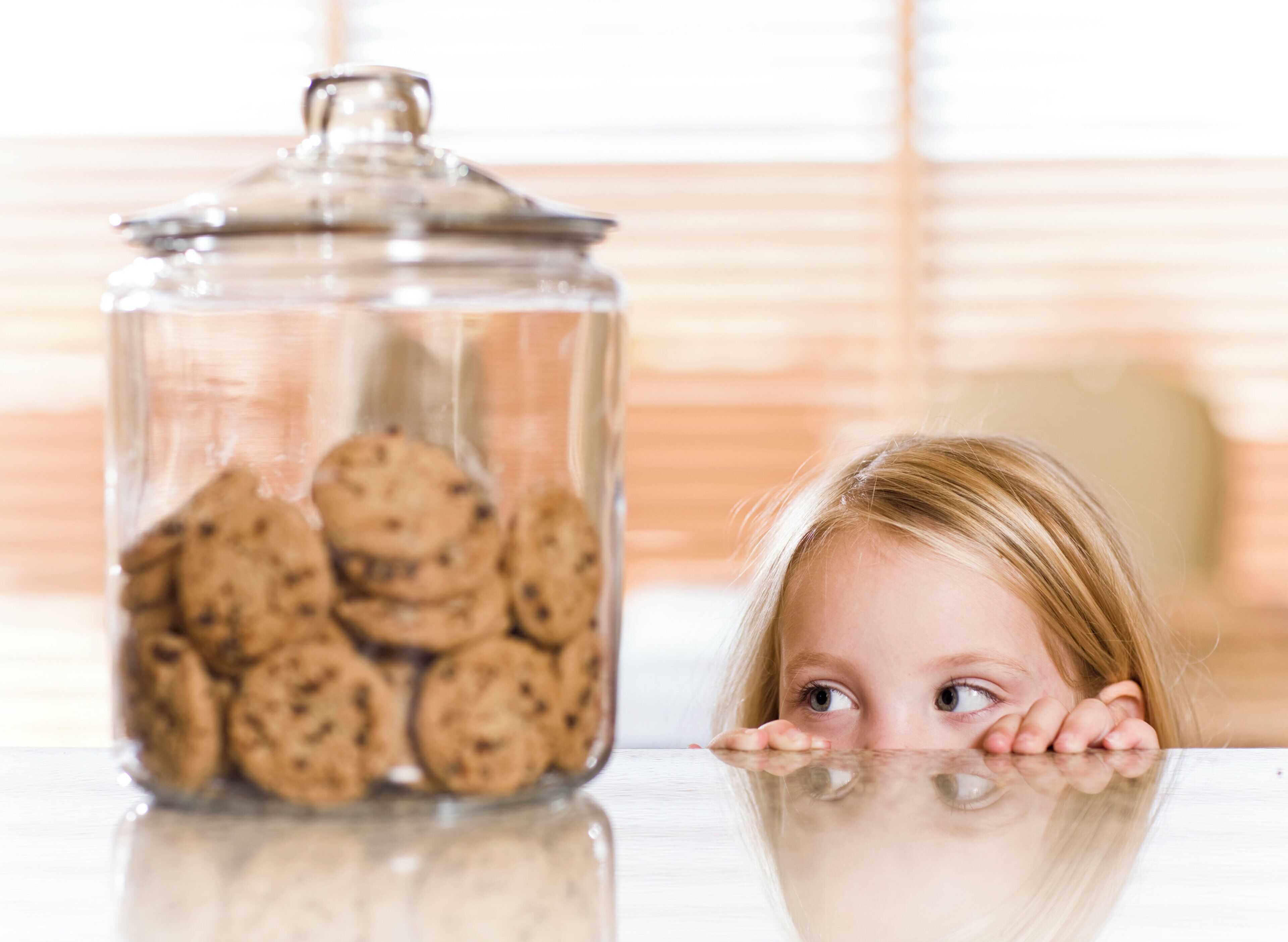 Un frasco de vidrio lleno de galletas sobre una superficie reflectante.