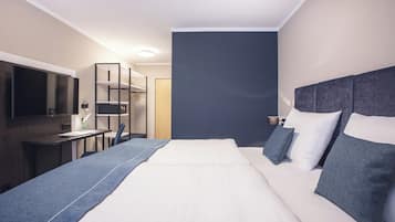 A modern hotel room with a large bed, a desk, a chair, and a TV.