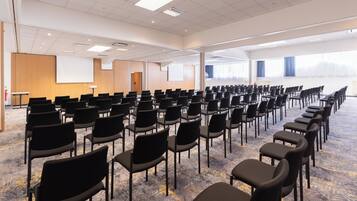 Ein Konferenzraum mit Reihen schwarzer Stühle, einer Projektionsleinwand und einem Teppichboden.