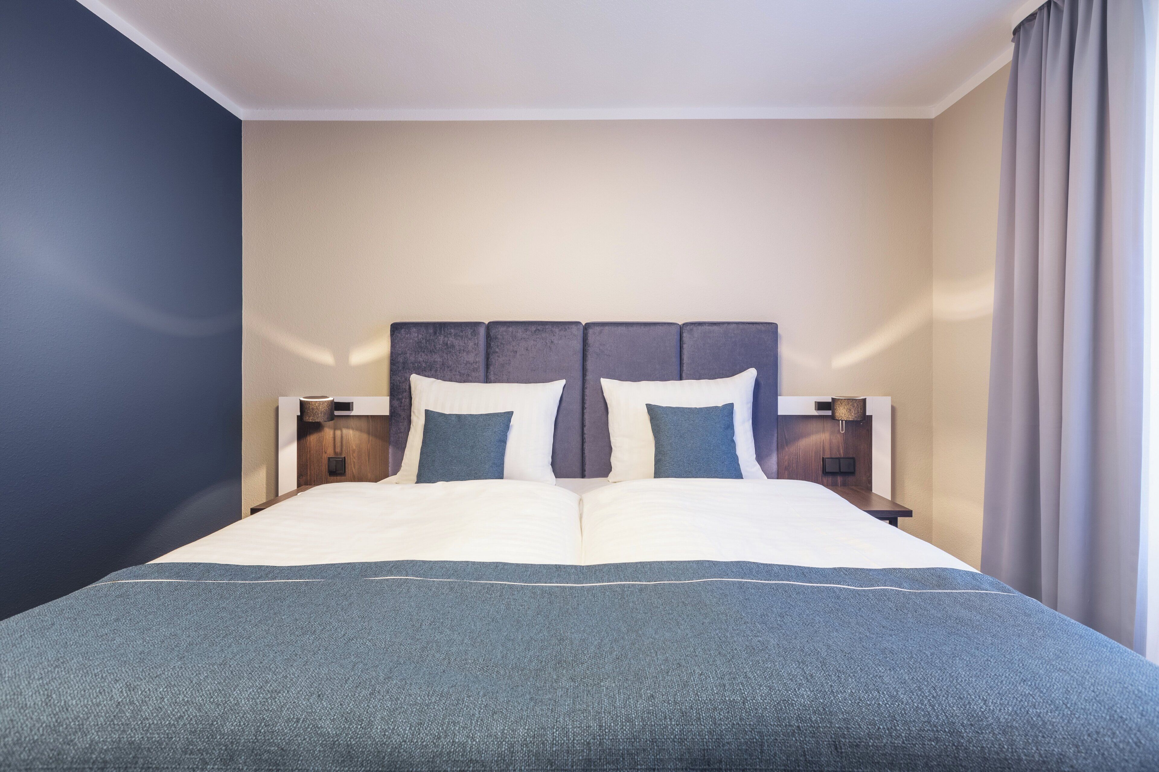 Habitación de hotel con una cama grande, dos mesitas de noche y una ventana con cortinas.