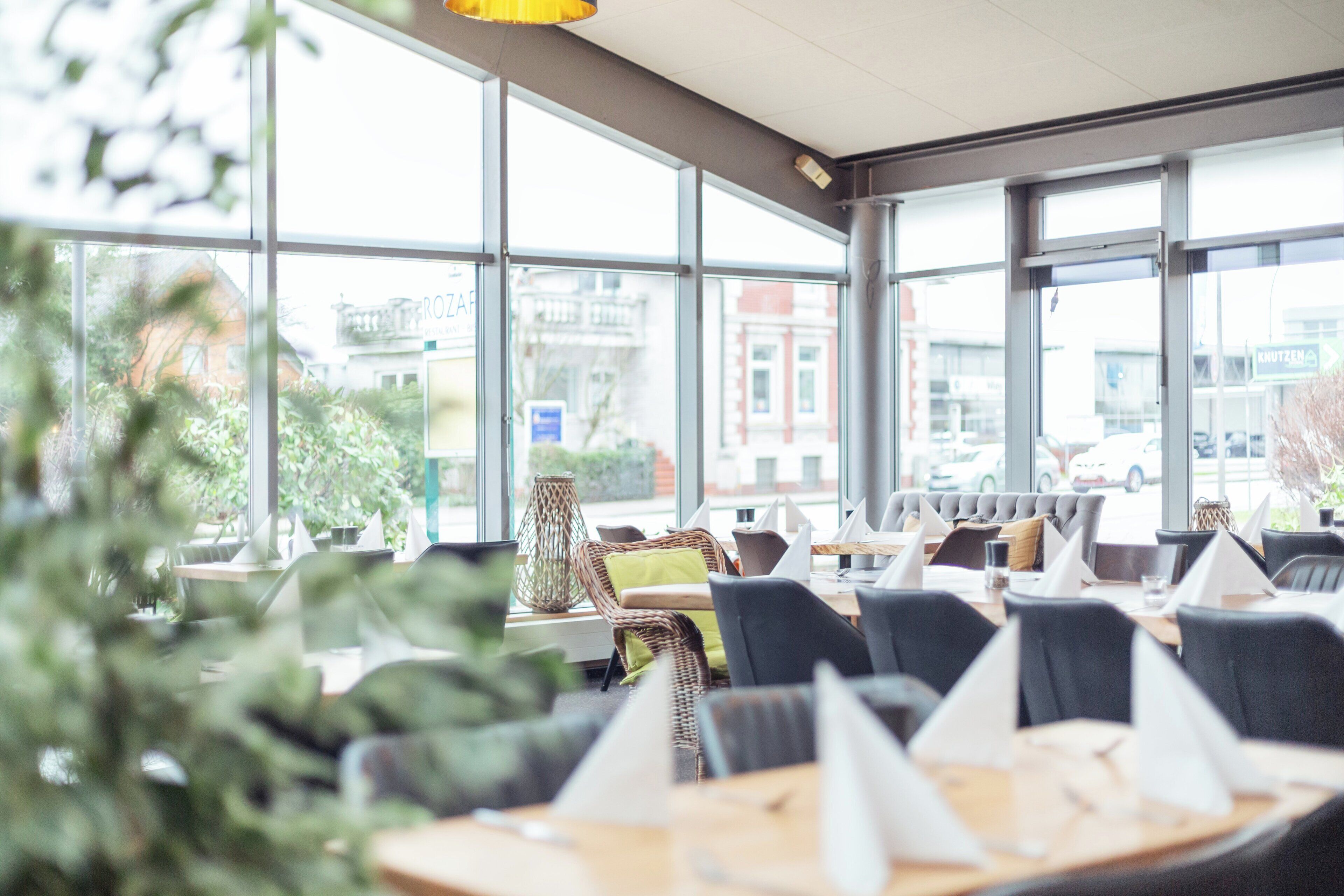 Un restaurante moderno con amplios ventanales, mobiliario de mimbre y mesas ordenadas.