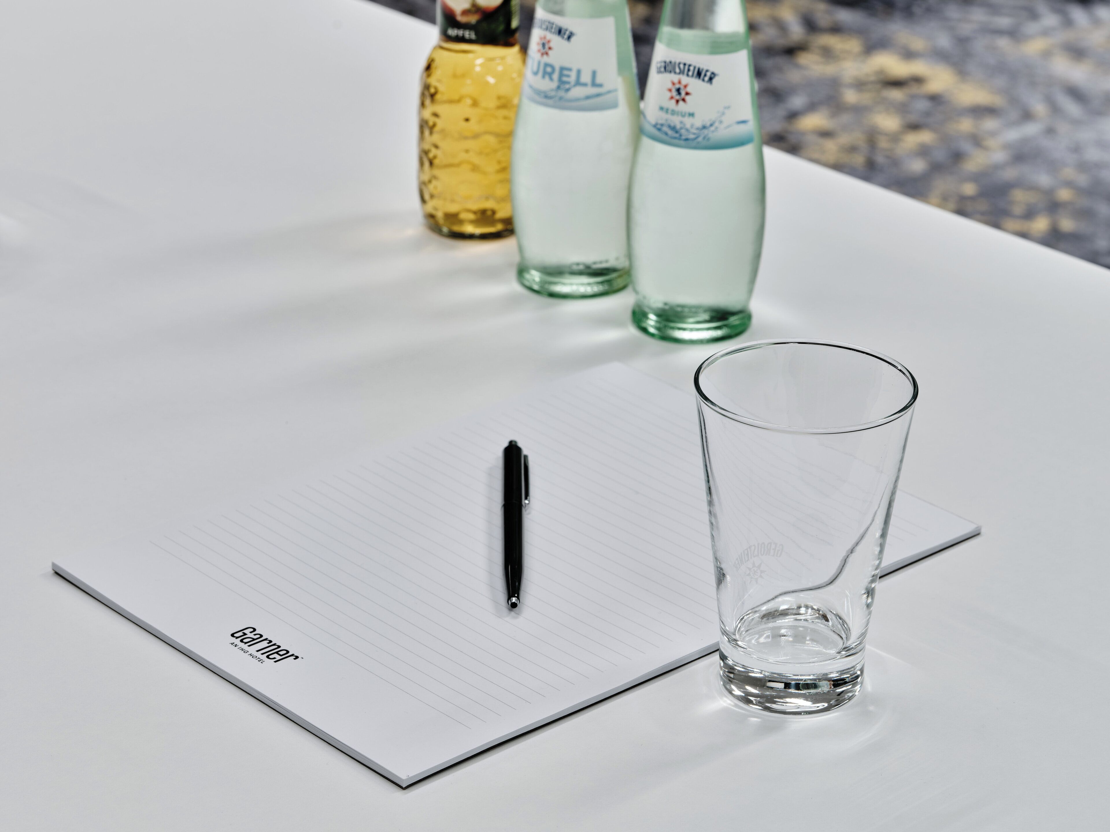 Un cuaderno con un bolígrafo y un vaso sobre una mesa.