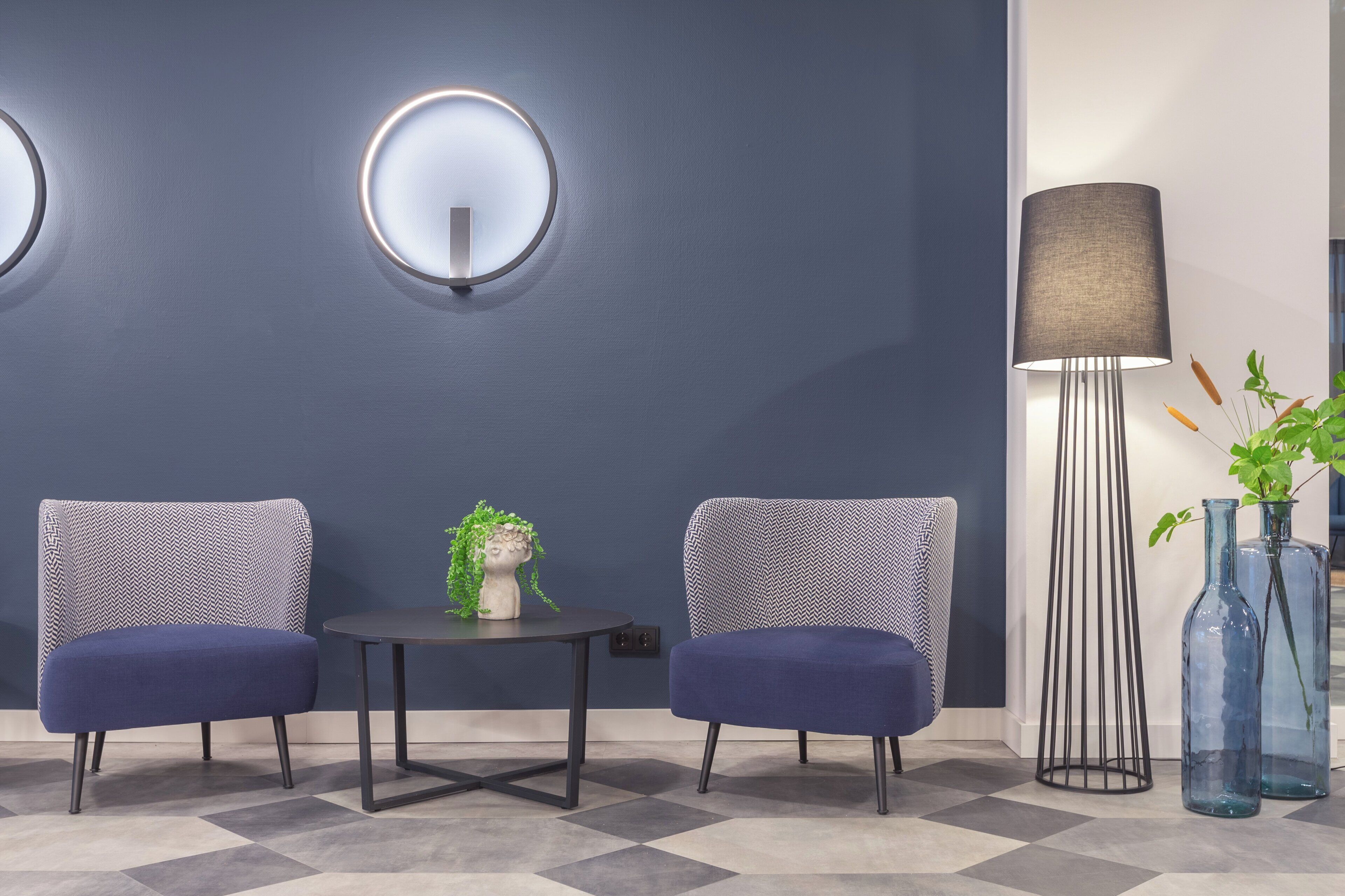 A modern room with two upholstered chairs, a round table, a tall floor lamp, and decorative vases.