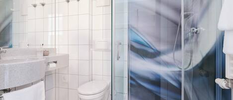 Un baño moderno con ducha envuelta en vidrio, inodoro blanco y lavamanos de granito.