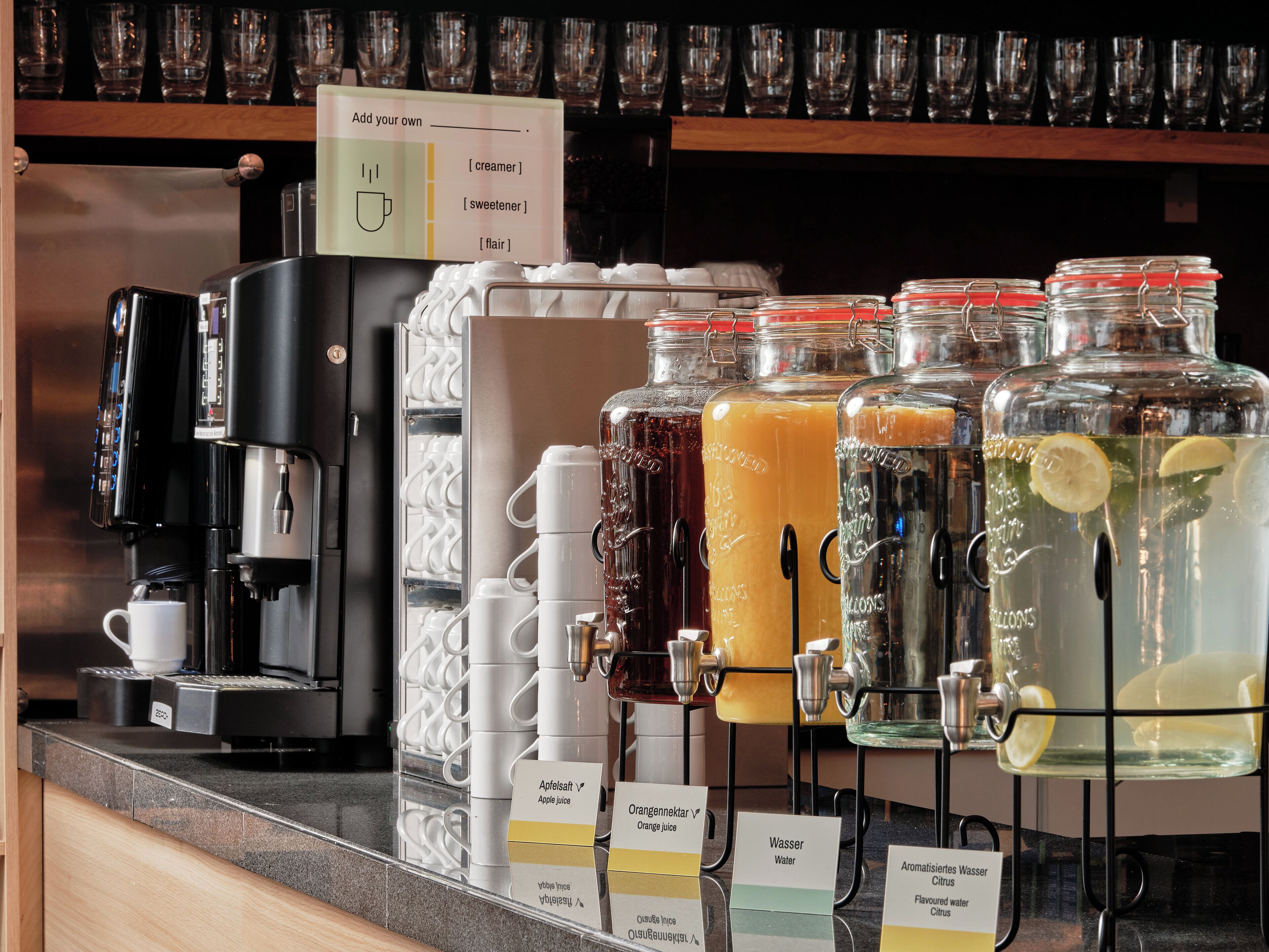 A coffee station with a coffee machine, multiple beverage dispensers, and labeled cups.