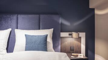 Habitación de hotel con una cama grande, una mesita de noche con lámpara y un cabecero oscuro.