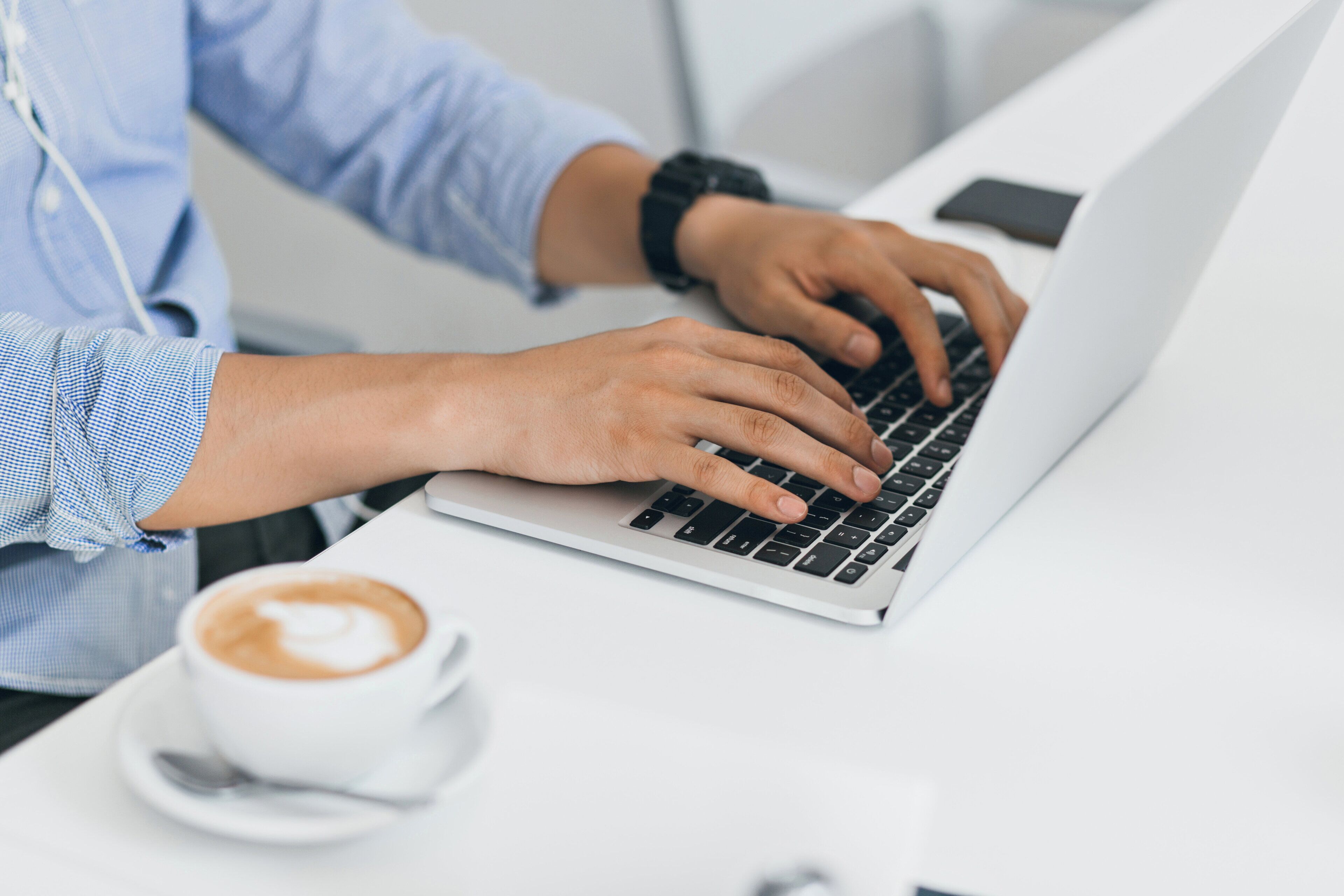 A person typing on a laptop with a cup of coffee on the table.