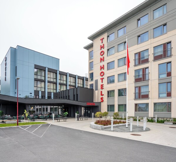 Ein modernes Hotel mit einem gut sichtbaren 'THONHOTELS'-Schild, Sitzgelegenheiten im Freien und einem Parkplatz.