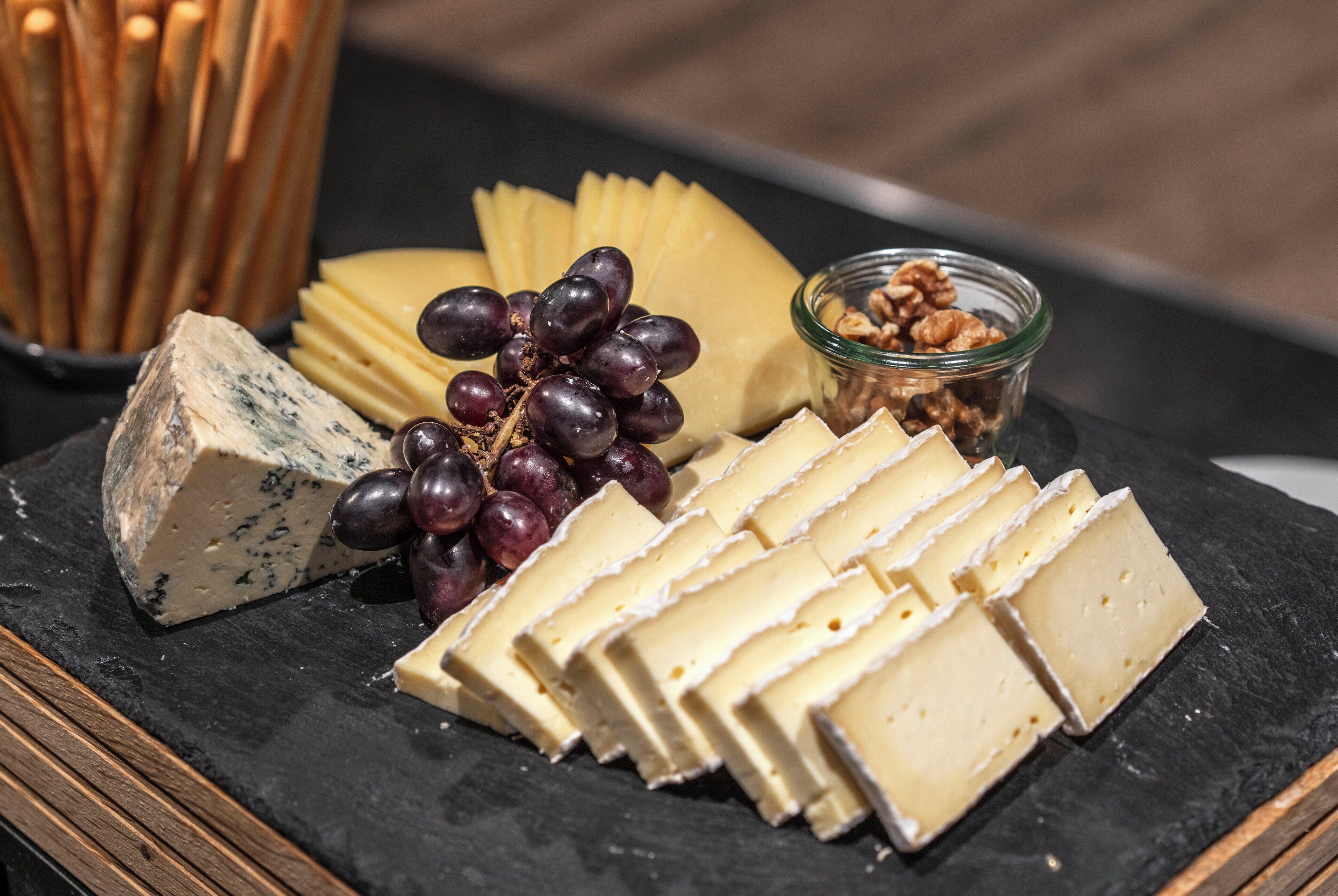 A cheese board with various cheeses, grapes, and nuts on a slate board.