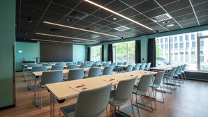 A conference room with rows of tables and chairs, large windows, and a projector screen. - Thon Hotel Brønnøysund (Brønnøy)