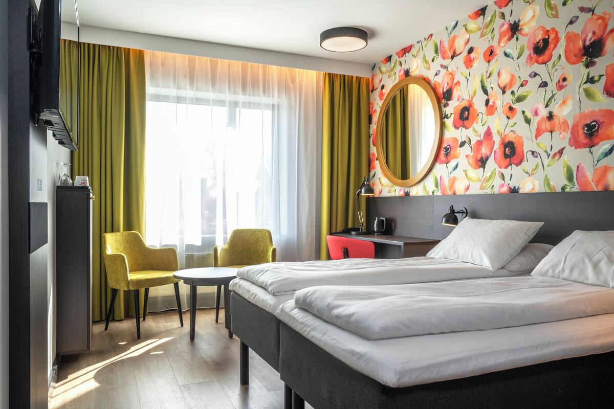 A hotel room with a bed, a desk, a chair, a mirror, and a window with curtains.