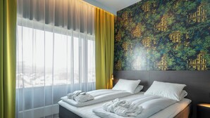 A hotel room with a bed, two towels, a window with sheer curtains, a wall with a patterned wallpaper, and a nightstand with a lamp. - Thon Hotel Brønnøysund (Brønnøy)
