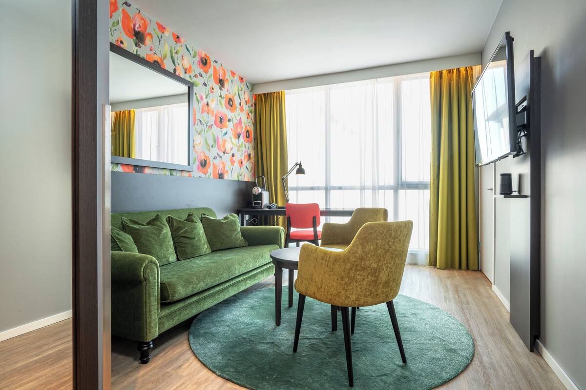 A modern living room with a green sofa, yellow armchairs, a round coffee table, and a large mirror on the wall.