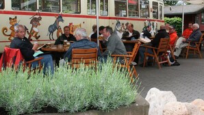 Een restaurant met terras, een oude bus ingericht als eetruimte, en gasten die van hun maaltijd genieten.