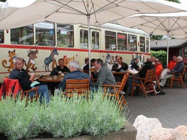 A restaurant with outdoor seating, a vintage bus as a dining area, and patrons enjoying their meals. - AKZENT Hotel Stadt Bremen (Beverungen)