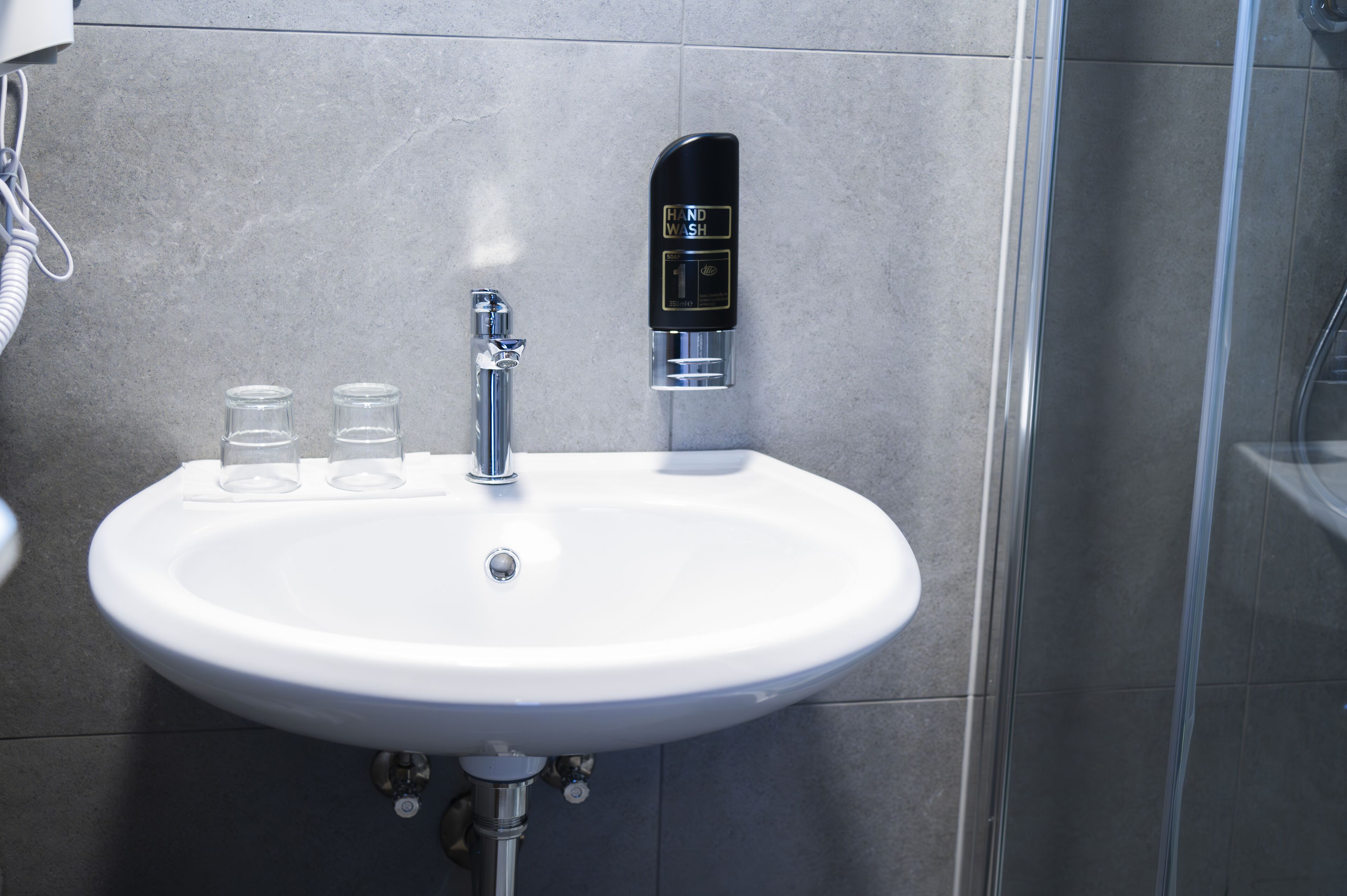 A white bathroom sink with a chrome faucet, a hand soap dispenser, and two clear glasses on the countertop.