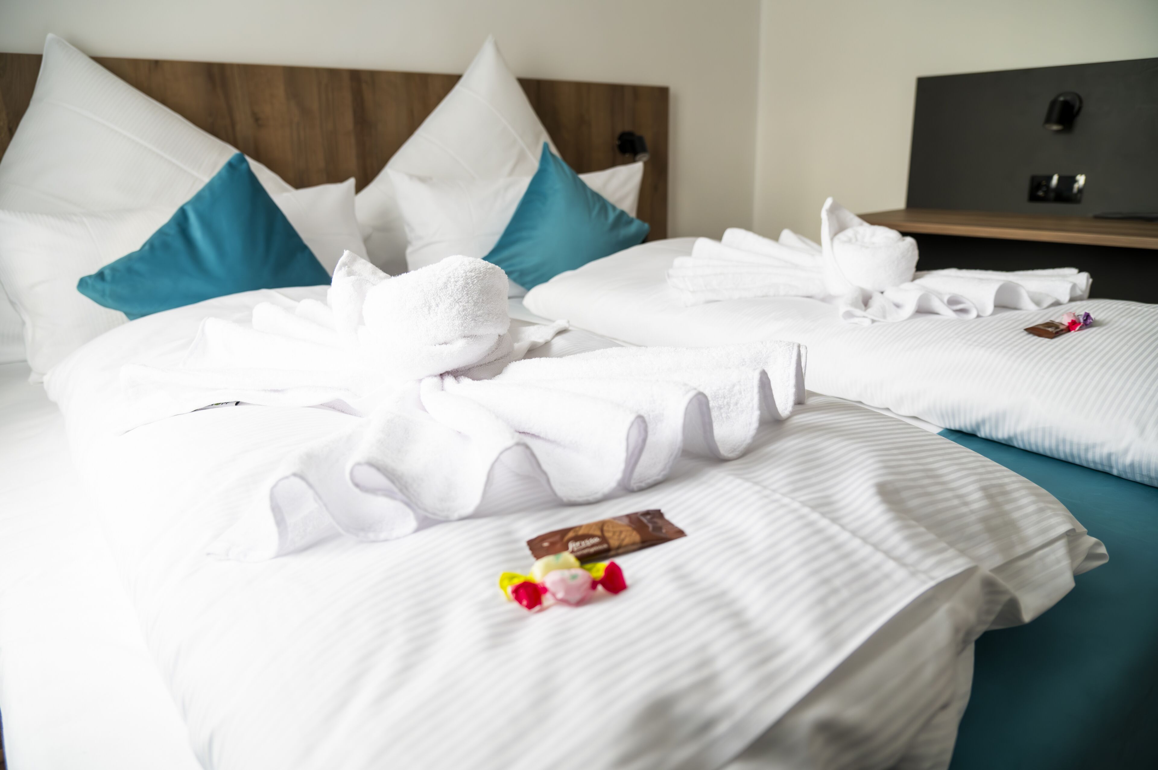 A hotel room with two beds, each with white linens, teal pillows, and a wooden headboard.