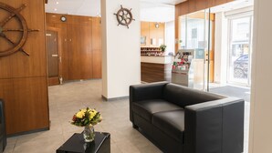 A reception area with a wooden wall, a black leather sofa, and a vase with flowers. - Hotel Hansa (Stuttgart)