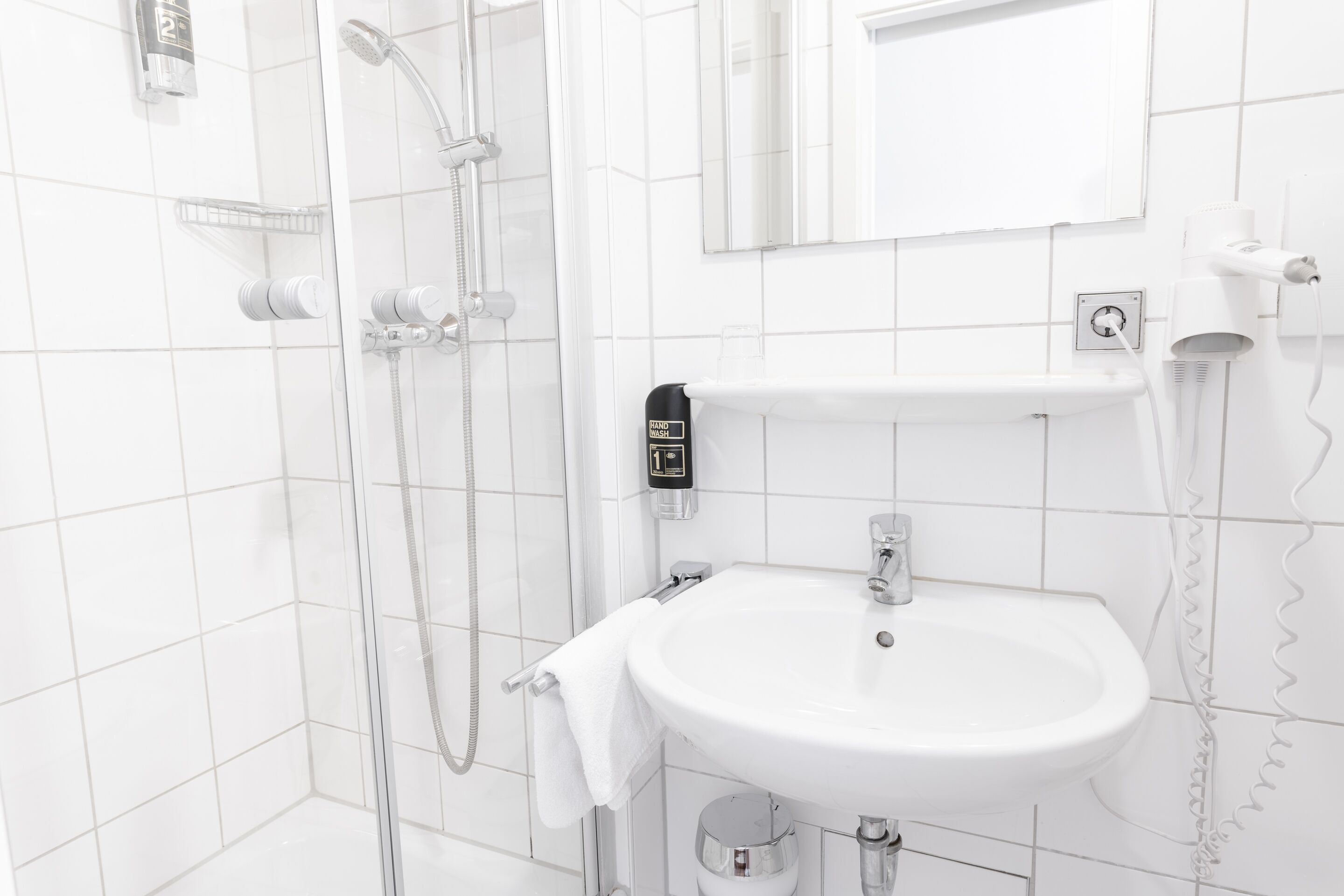 Un baño moderno con ducha de vidrio, lavamanos blanco y espejo sobre el lavamanos.