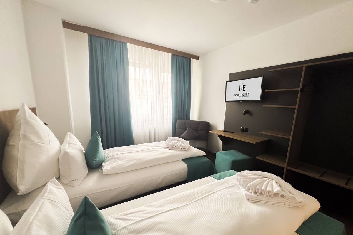 Una habitación de hotel con dos camas individuales, un escritorio, una silla, un televisor y un armario.