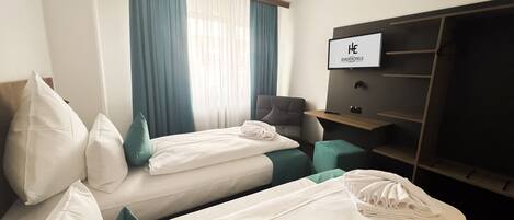 Una habitación de hotel con dos camas individuales, un escritorio, una silla, un televisor y un armario.