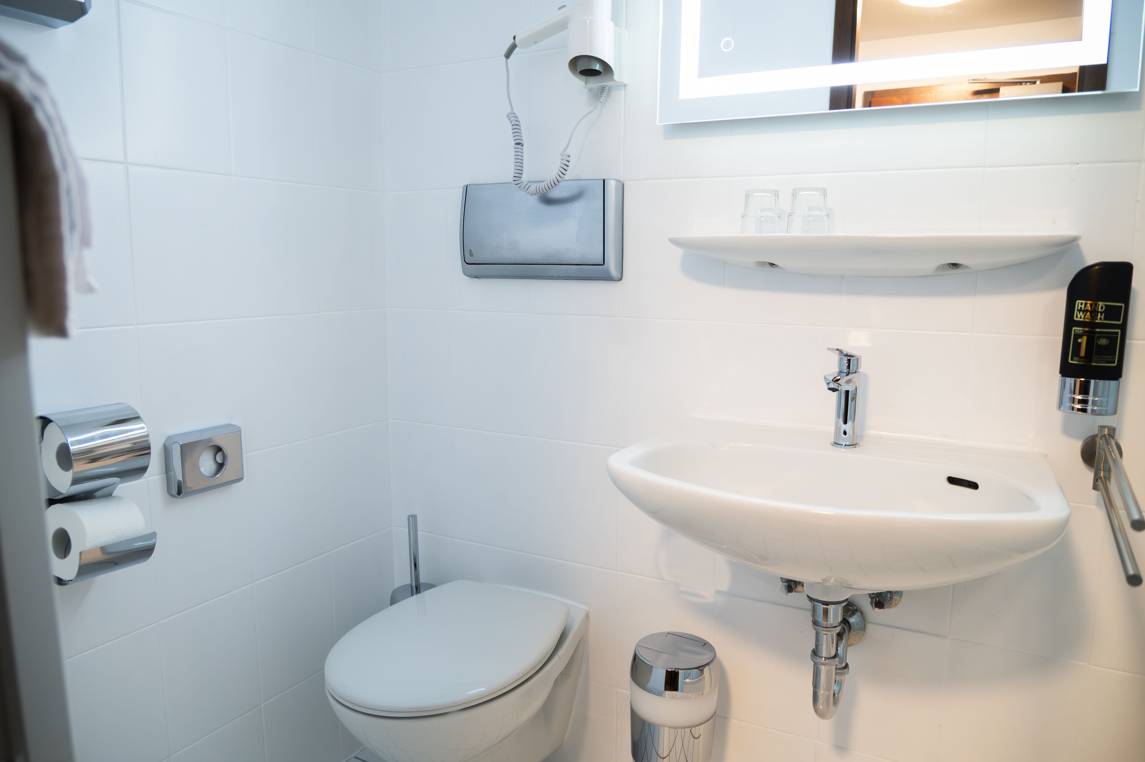 A bathroom with a toilet, sink, towel dispenser, and a mirror.