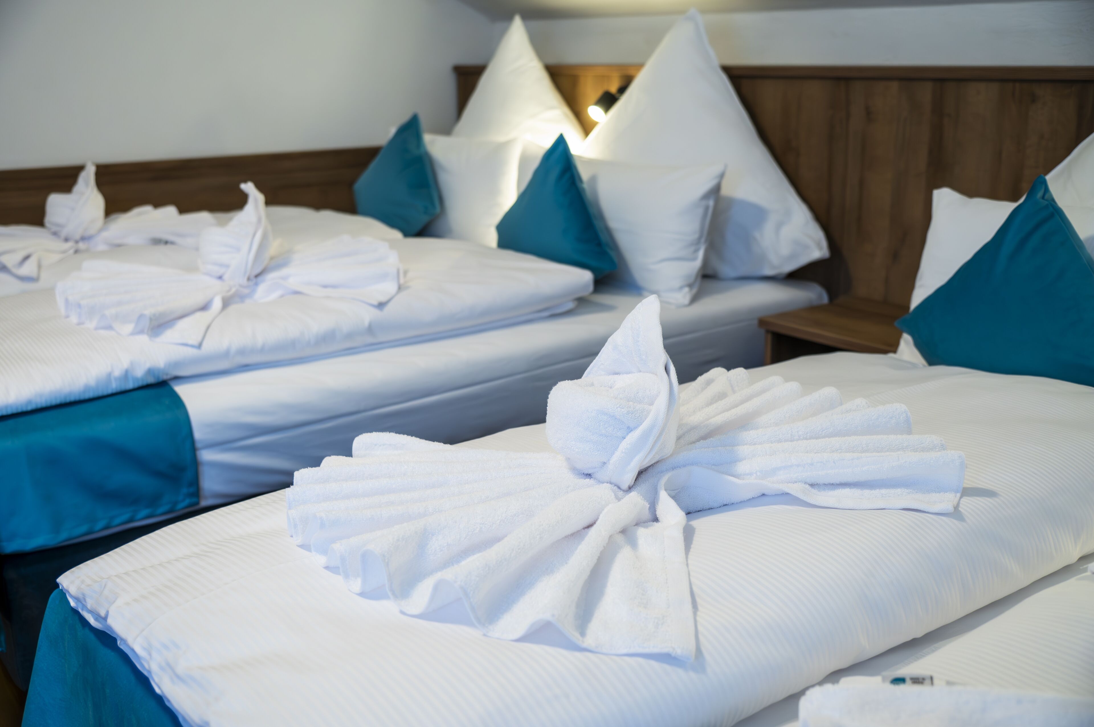 Habitació d'hotel amb dos llits, cadascun amb tovalloles blanques perfectament plegades i almoinades turquesa.