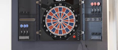 Un jeu de fléchettes fixé au mur, avec un étui pour fléchettes et des fléchettes à côté.