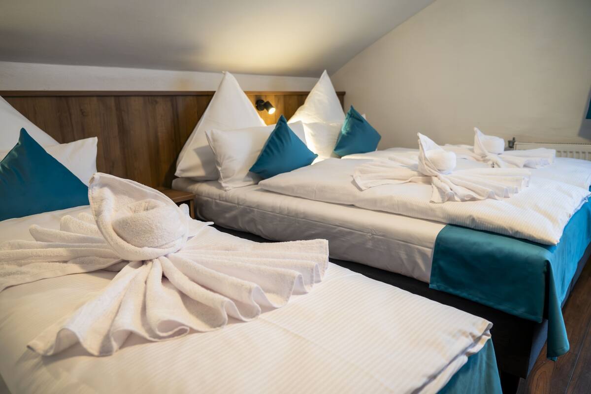Habitación de hotel con dos camas, cada una con ropa blanca y almohadas color turquesa.