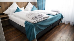 A neatly made bed with white and teal bedding, a wooden headboard, and a wooden floor. - Hotel Hansa (Stuttgart)