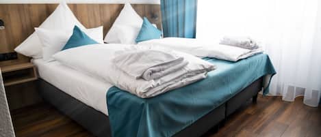 Una cama bien hecha con ropa de cama blanca y verde azulado, un cabecero de madera y piso de madera.