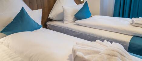 Quarto de hotel com duas camas, cada uma com roupa de cama branca e almofadas azuis.