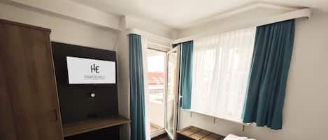 A hotel room with a bed, a bench, a TV, and a view of the outside.