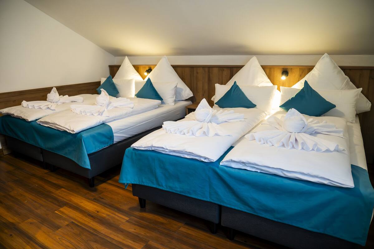 Dos camas individuales con ropa de cama color turquesa y almohadas blancas, cabeceros de madera y piso de madera.
