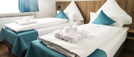Dos camas individuales con colchas color turquesa, almohadas blancas y cabeceros de madera.