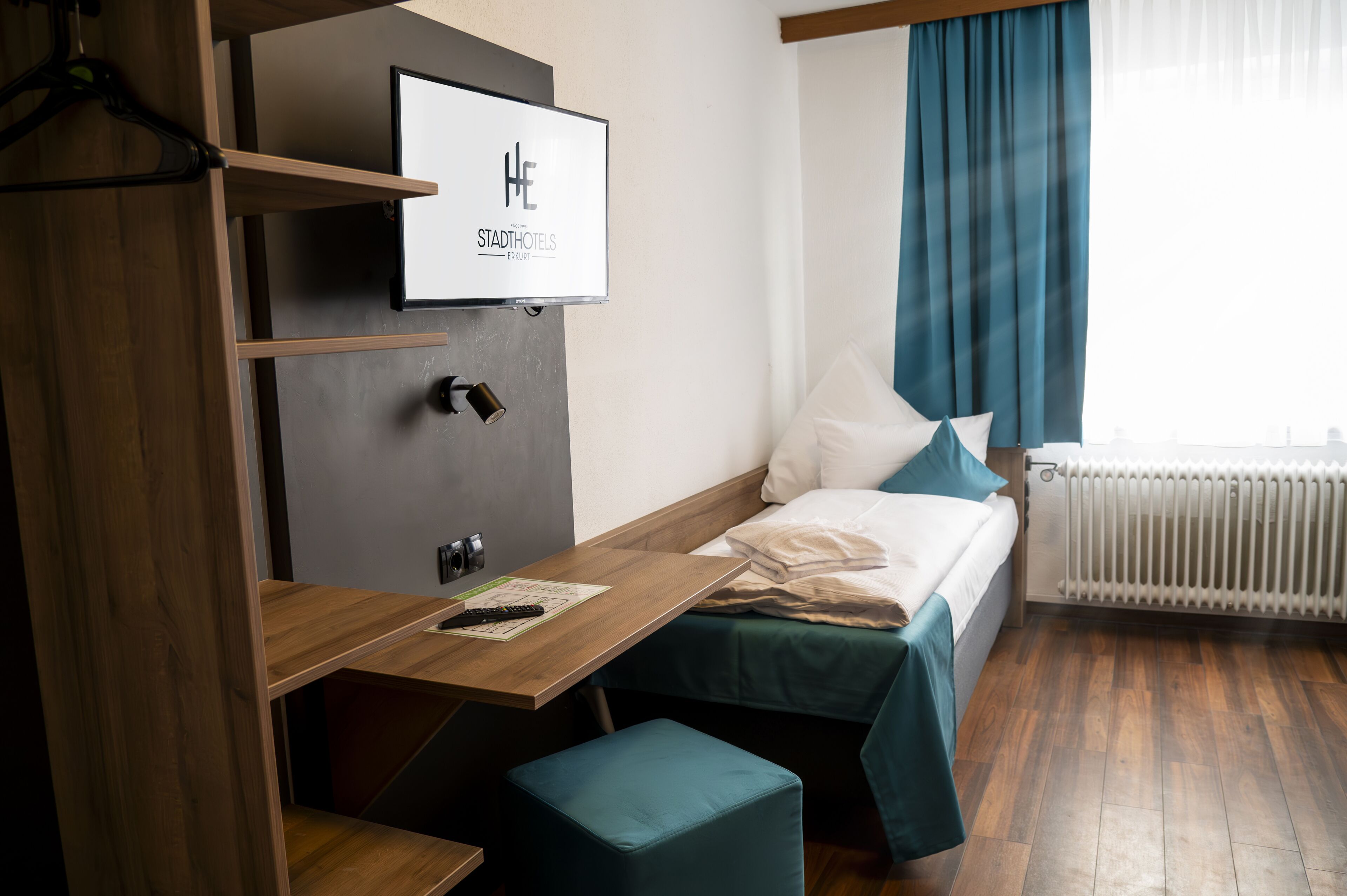 A hotel room with a bed, a desk, a TV mounted on the wall, and a window with curtains.