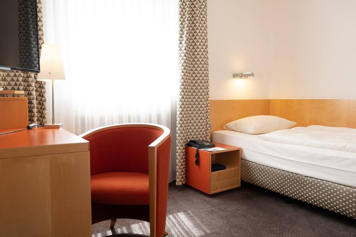 Una habitación de hotel con una cama, un escritorio con lámpara, una silla y un teléfono.