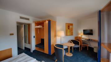 Habitación de hotel con cama, escritorio con silla, televisor y una pequeña mesa con otra silla.