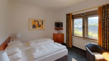 A hotel room with a bed, a television on a stand, a chair, and a window with curtains.