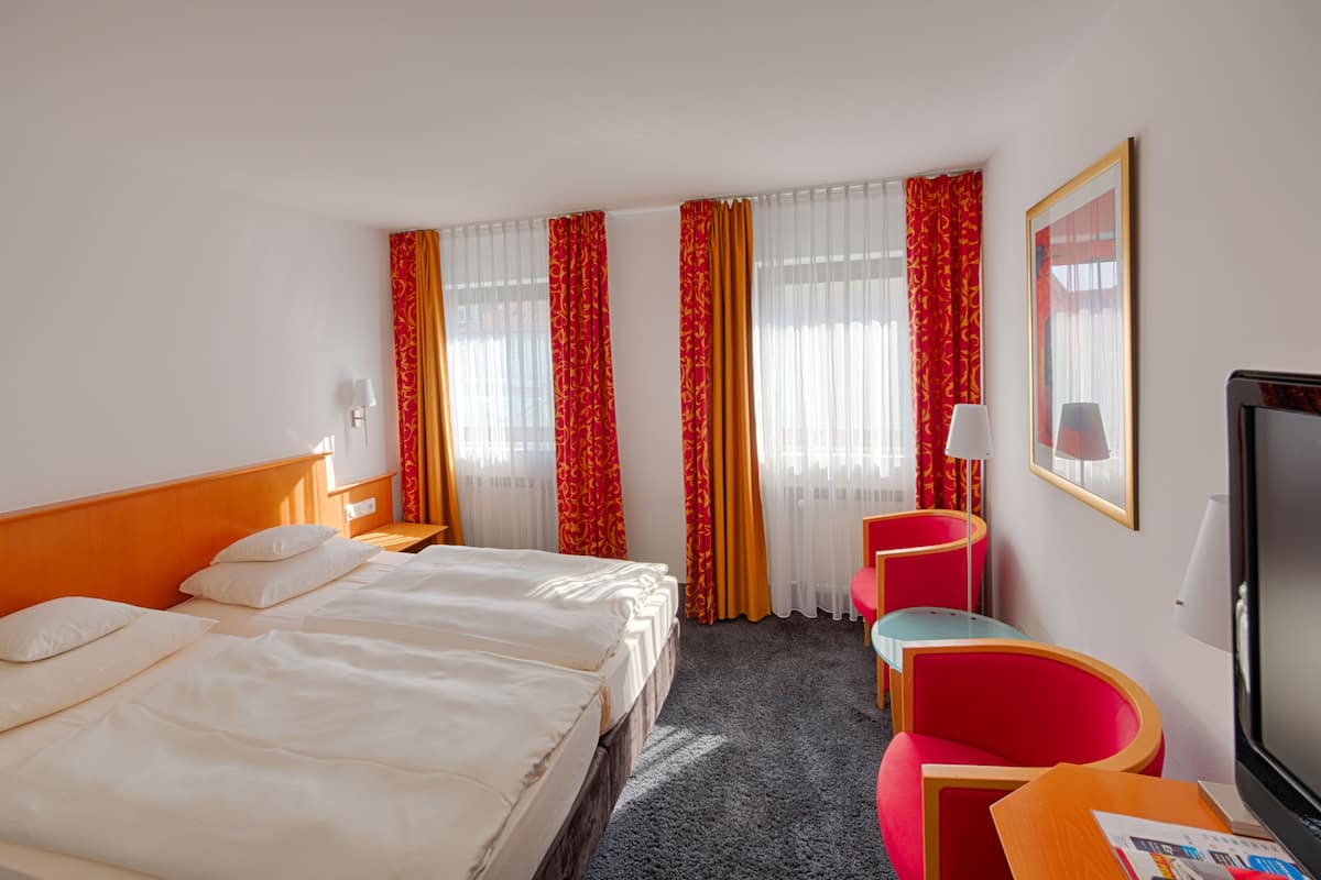 Una habitación de hotel con una cama, dos sillas, un escritorio y un televisor.