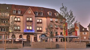 Een hotel met meerdere verdiepingen, balkons met bloembakken en een opvallend bord voor een restaurant.