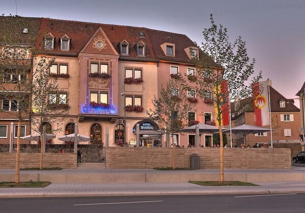 A hotel with multiple floors, balconies with flower boxes, and a prominent sign for a restaurant.