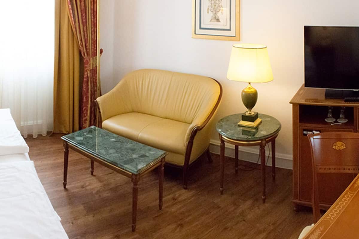 Une chambre d’hôtel avec deux lits, un canapé, une petite table, une télévision et des lampes.