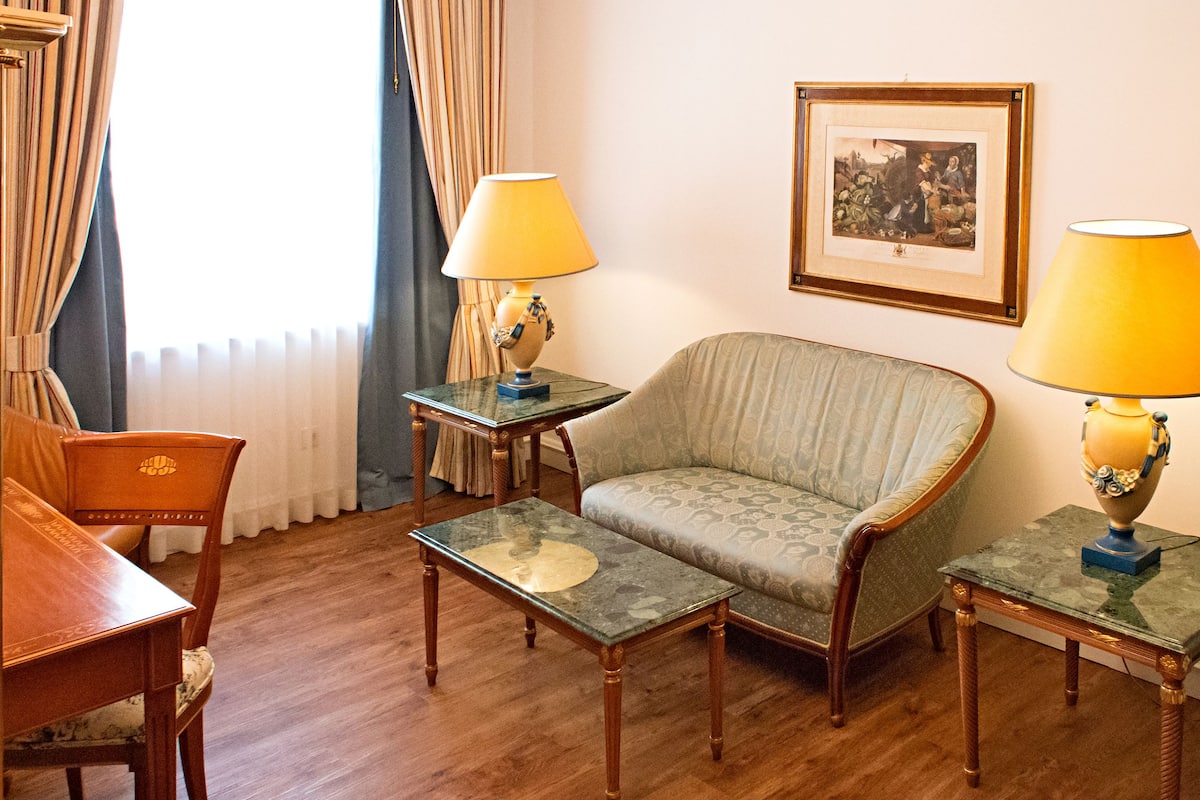 Une pièce comprenant un canapé, deux tables d’appoint avec des lampes, un fauteuil et un tableau encadré accroché au mur.