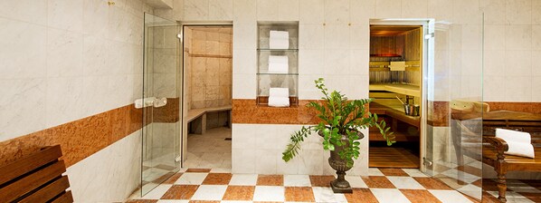 Baño de hotel con cabina de ducha de vidrio, suelo de mármol y banco de madera con una toalla.